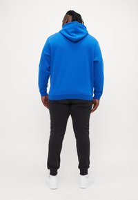 Camisola azul com bolso canguru frontal, cordão ajustável e punhos canelados, combinada com calças pretas e sapatilhas brancas.