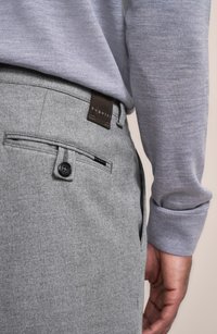 Graue Wollhosen mit glatter Textur, versehen mit einem Knopf und einem dezenten Logo-Tag auf der Gesäßtasche, kombiniert mit einem hellblauen Pullover.