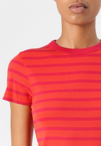 Top à manches courtes en coton, en rouge vif avec des rayures roses alternées, présentant un col rond et une coupe ajustée.