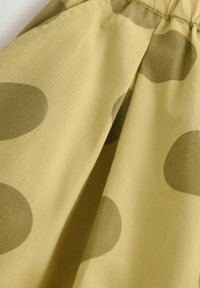 Tissu jaune pâle avec de grands pois verts olive aux bords doux et un détail froncé sur le bord supérieur.