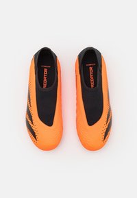 Oranssit jalkapallokengät mustilla yksityiskohdilla, joissa on sileä, teksturoitu päällinen ja tiukka istuvuus. Suunniteltu ketteryyttä ja nopeita liikkeitä varten.