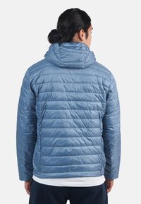 Giacca imbottita azzurro chiaro con cappuccio, caratterizzata da righe orizzontali trapuntate e una superficie liscia e lucida. La vista dal retro mostra una vestibilità comoda.
