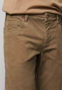 Brązowe spodnie z sztruksu z drobnymi, pionowymi prążkami, wyposażone w przednią kieszeń, zamek błyskawiczny i mały guzik z logo marki.