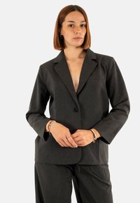 Blazer nero a righe sottili con rever a punta, chiusura a un bottone e due tasche frontali. Realizzato in tessuto testurizzato.