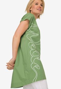 Zelená tunika s krátkým rukávem, zdobená velkým bílým nápisem na přední straně. Vyrobena z lehkého materiálu s volným střihem.