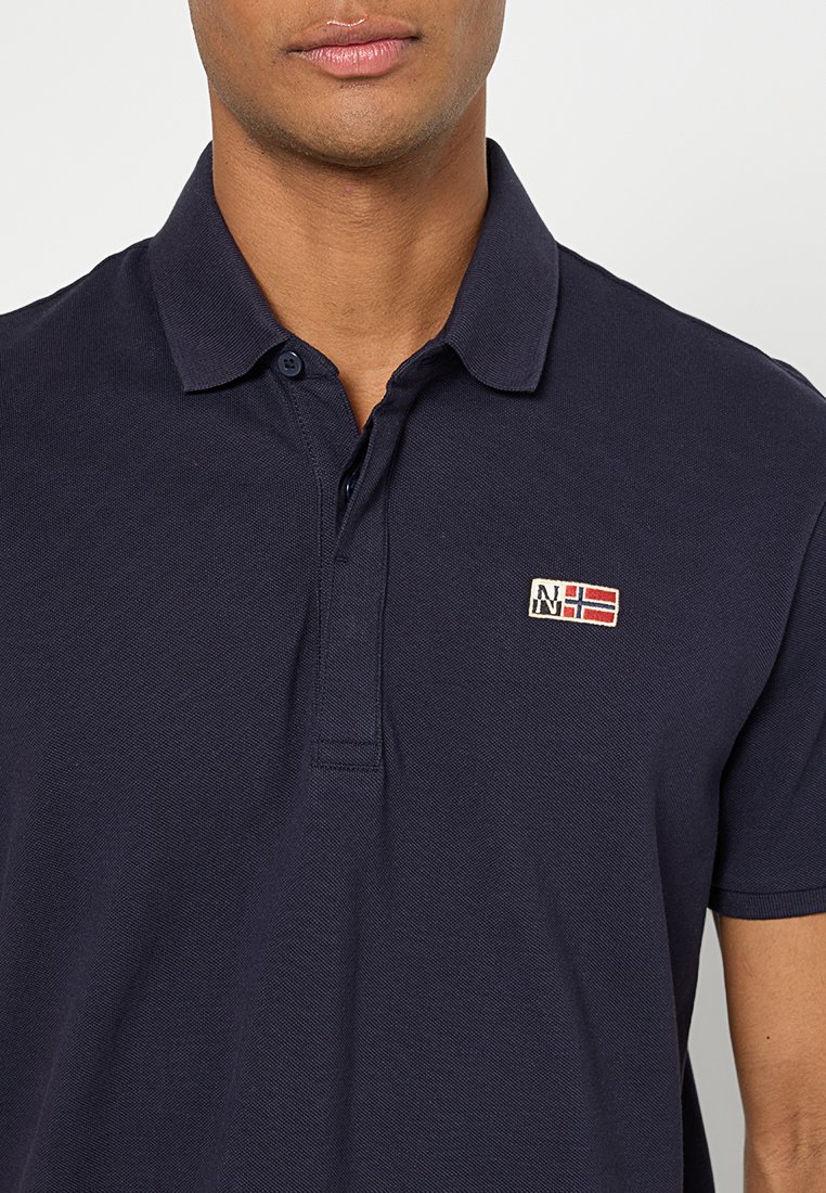 Polo shirt bleu marine en coton texturé, avec un col à deux boutons et un patch logo brodé sur la poitrine gauche.