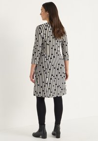 Svart och vit mönstrad klänning med trekvartsärmar, åtsittande form, sidofickor och en slät yta. Kombinerad med svarta leggings och ankelskor.