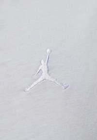 Tessuto bianco con logo Jumpman ricamato in rilievo di colore grigio chiaro, che rappresenta la silhouette di una figura che salta con un pallone da basket.