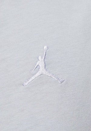 Tessuto bianco con logo Jumpman ricamato in rilievo di colore grigio chiaro, che rappresenta la silhouette di una figura che salta con un pallone da basket.