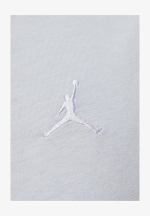 Tessuto bianco con logo Jumpman ricamato in rilievo di colore grigio chiaro, che rappresenta la silhouette di una figura che salta con un pallone da basket.
