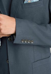 Dunkelblazer aus strukturiertem Stoff, mit vier Knöpfen an den Manschetten und einem dekorativen Taschentuch mit floralem Muster.