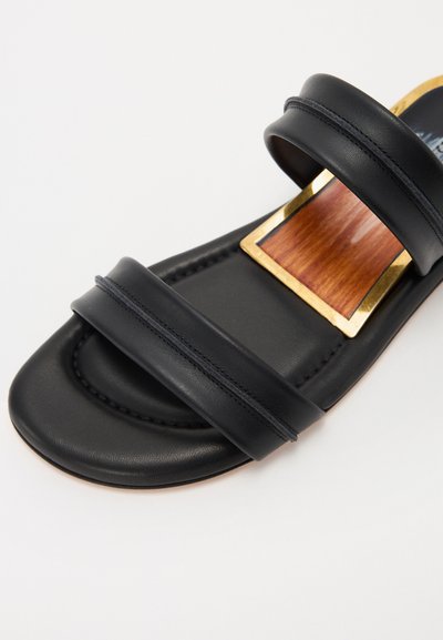 Sandały deslizantes de cuero negro con dos correas horizontales, una textura suave y un acento de madera bordeado por hardware dorado.