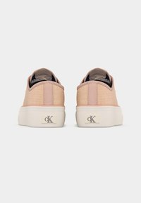 Ζευγάρι ανοιχτό ροζ χαμηλά αθλητικά παπούτσια με χοντρές λευκές σόλες, με ορατό λογότυπο Calvin Klein στη φτέρνα, φωτογραφημένα από πίσω σε απλό φόντο.