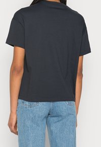 Mörk marinblå t-shirt, korta ärmar, avslappnad passform, bomullsmaterial, enkel rund halsringning, kombinerad med ljusblå slitna jeans.