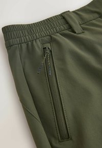 Olivengrüne Hose mit elastischem Bund und seitlicher Reißverschlusstasche. Hat eine glatte Textur und einen geraden Schnitt, mit verstärkten Steppnähten.