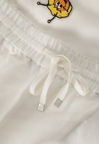 Witte katoenen shorts met elastische tailleband en trekkoord, met een gele bijborduursel op de voorkant en metalen hardware-accenten.