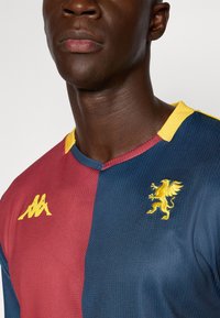 Bordeaux- og marinefarvet fodboldtrøje med gul krave; har en struktureret overflade, Kappa-logo og et gyldent løvemotiv på brystet.