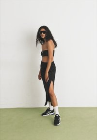 Fekete pánt nélküli top fekete szoknyával, oldalsó hasítékkal párosítva. Fehér zoknik és fekete sportcipők fehér talppal. Sötét napszemüveg viselve.
