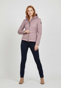 Light purple puffer jacket with horizontal quilted design, attached hood, front zipper, and logo accent. Worn over navy pants and beige boots.