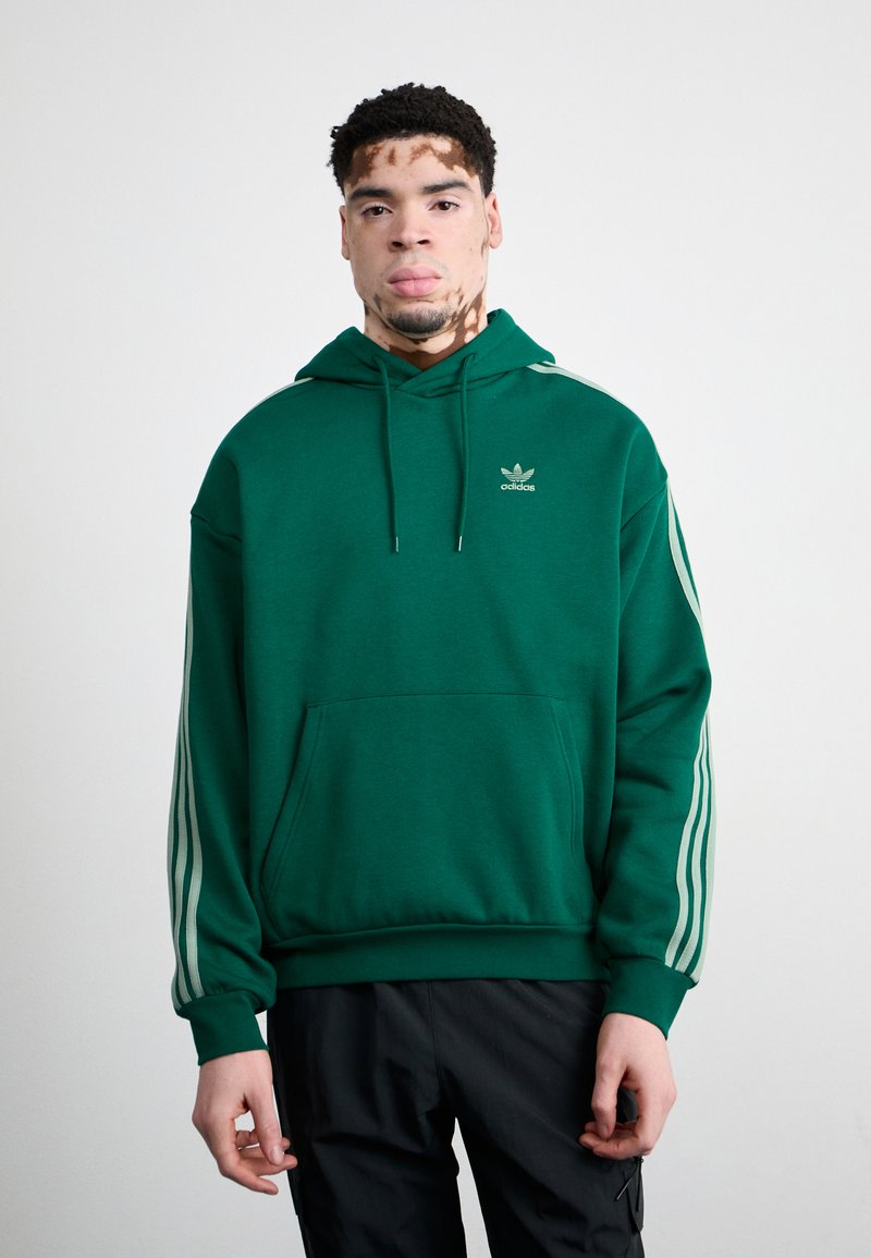 Sweatshirt verde com um bolso frontal, capuz com cordão e três riscas brancas nas mangas. Apresenta um pequeno logótipo no peito.