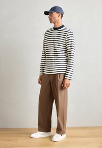 Chemise à rayures à manches longues en crème et bleu marine, associée à un pantalon marron et des baskets blanches. Dotée d'un col rond et d'une coupe décontractée.