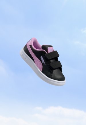 Μαύρο και ροζ αθλητικό παπούτσι Puma με λευκή σόλα και δύο μαύρα λουριά βέλκρο που αιωρούνται μπροστά σε φόντο μπλε ουρανού.