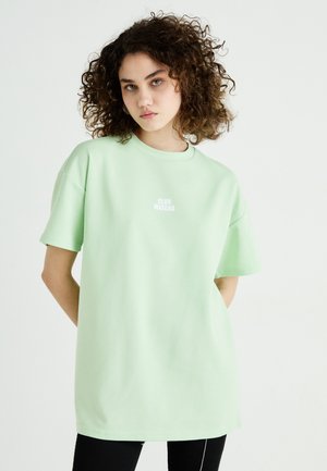 Lys grønn oversized t-skjorte laget av myk bomull, med korte ermer og runde hals, med "CLUB MATCHA" trykket i hvitt på brystet.