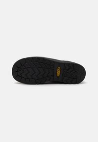 Semelle de botte en caoutchouc noir avec des crampons profonds et multidirectionnels pour une adhérence optimale. Elle présente un logo en relief et une large surface pour plus de stabilité.