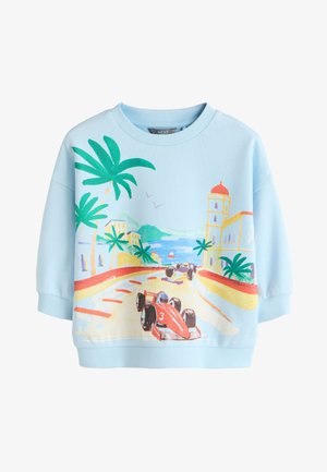 Hellblauer Pullover mit einer Küstenstraßen-Rennszene mit roten und schwarzen Rennwagen, Palmen, Gebäuden und Vögeln am Himmel.
