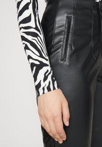 Svarta läderbyxor med sidoficka, i kombination med en långärmad topp med svart-vitt zebramönster.