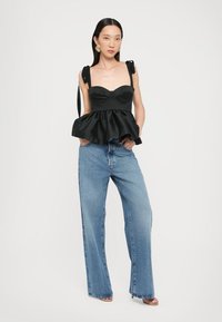 Melna peplum tops ar polsterētu krūšu daļu, platām siksnām ar lokiem un gludu tekstūru. Kombinēts ar augsto jostasvietu, brīvi pieguļošiem ziliem džinsiem.