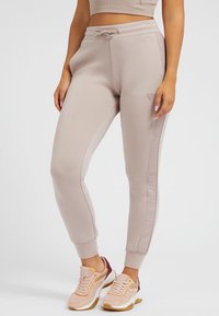 Hellbeige Jogginghosen mit elastischem Bund und Kordelzug, ausgestattet mit seitlichen Streifen und gerippten Bündchen. Kombiniert mit pastellfarbenen Sneakers.