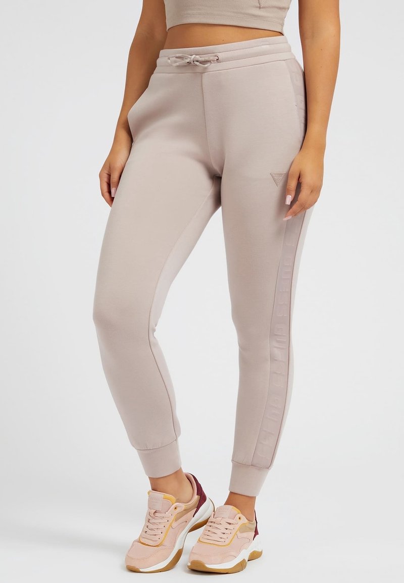 Hellbeige Jogginghosen mit elastischem Bund und Kordelzug, ausgestattet mit seitlichen Streifen und gerippten Bündchen. Kombiniert mit pastellfarbenen Sneakers.