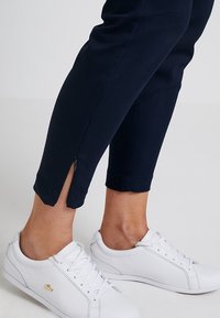 Marina blå, cropped byxor med sidsidizip, tillverkade av mjukt tyg, parat med vita snörskor med en diskret logotyp.