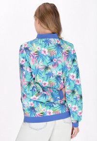 Kurtka bomber z kwiatowym wzorem, prezentująca żywe tropikalne kolory: zielenie, różowe i niebieskie. Z ribbowanymi mankietami i kołnierzem, gładka tekstura materiału.
