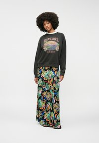Sweatshirt noir avec un graphique "Ripcurl Hawaii" et une jupe maxi florale colorée présentant un motif de feuilles vibrantes.