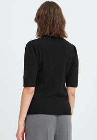 Sort kortærmet sweater med ribkant ved kanten og manchetterne, lavet af blødt materiale. Designet har en høj halslinje og en tætsiddende silhuet.