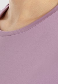 Lilafarbene Baumwoll-T-Shirt mit glatter Textur, Rundhalsausschnitt und einem klaren, schlichten Design. Nahaufnahme hebt die sanfte Farbe hervor.