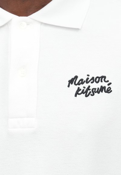 Biele polo tričko s štruktúrovanou tkaninou, s trojicou gombíkov na zapínanie a vyšívaným čiernym logom "maison kitsuné" na ľavej hrudi.