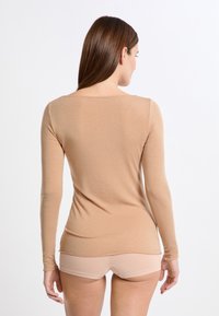 Top de manga larga en tejido de punto beige, con cuello redondo y silueta ajustada, combinado con pantalones cortos beige a juego.