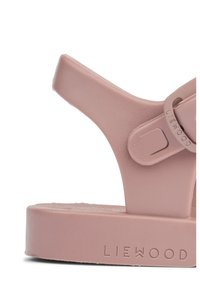 Różowa gumowa sandałka z szerokim paskiem, teksturowaną podeszwą i regulowanym paskiem z klamrą. Z boku znajduje się wytłoczone logo marki.