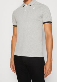 Polo grigio con colletto, con strisce accentate in blu navy e giallo sulle maniche e un piccolo logo sulla parte sinistra del petto.