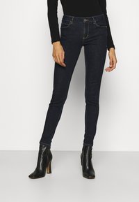 Mörkblå skinny jeans i denim med en slät yta, femfickorsdesign och guldstickningar. Bärs med svarta klackstövlar.