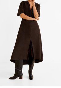 Brązowa sukienka z krótkim rękawem i dekoltem w serek, z przodu z rozcięciem i asymetrycznym hemem. W połączeniu z czarnymi botkami do kolan.