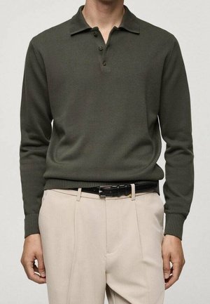 Zielony ribbowany sweter z kołnierzykiem i trzema guzikami, w połączeniu z jasnobeżowymi spodniami i czarnym paskiem.