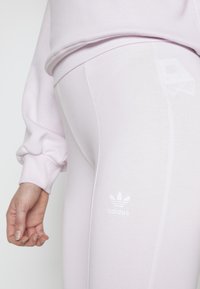 Svetlo roza športne legice, narejene iz mehke tkanine, z belim logotipom Adidas ter brezšivnim dizajnom s stranskimi šivi.