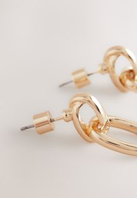 Gold metal earrings featuring a linked chain design, with a smooth texture and a cylindrical backing. Ideal for casual or formal wear.