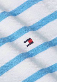 Tela de algodón con rayas horizontales blancas y azul claro. Se observa un pequeño logo bordado con rectángulos rojos y negros.