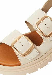 Beige sandal with two adjustable straps, gold-tone buckles, a smooth upper, and a brown cushioned footbed with a chunky white sole.
