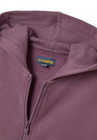 Sudadera con cremallera morada y un cuello interior texturizado, que presenta una etiqueta azul en contraste. La tela parece suave y tiene un acabado liso.